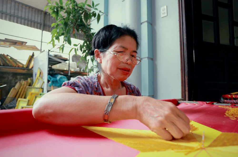 Bà Hải (59 tuổi, Thường Tín) là một người thợ lành nghề trong làng với hơn 40 năm thêu cờ. Bà luôn chăm chút từng đường kim, mũi chỉ để thêu lên những ngôi sao vàng đẹp nhất. anh-chup-man-hinh-2025-04-28-luc-134521.png